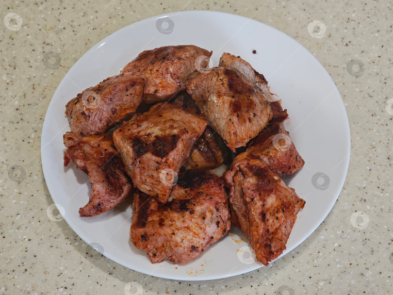 Скачать На белой тарелке кусочки мяса, приготовленные на электрическом гриле в помещении на кухне. На белой тарелке лежит мясо, приготовленное на электрическом гриле в закрытом помещении кухни. фотосток Ozero