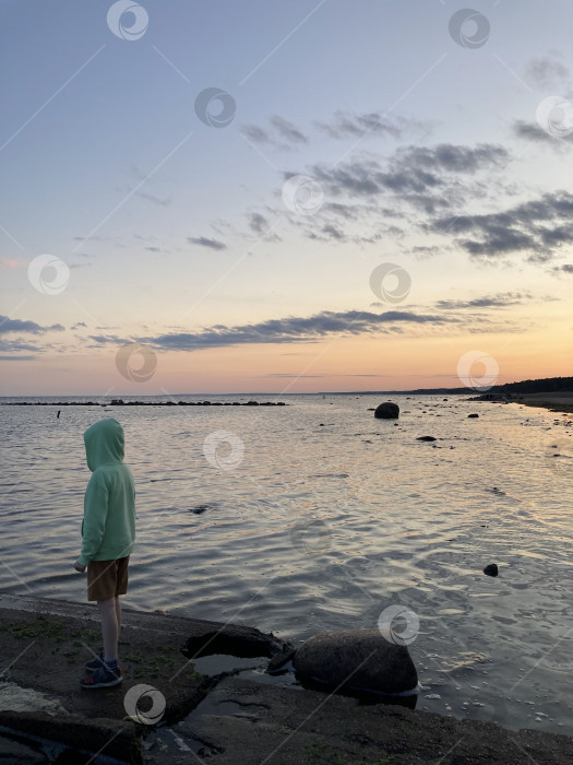 Скачать Море на закате. Мальчик в толстовке с капюшоном смотрит на горизонт фотосток Ozero