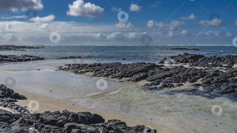 Скачать Груды черных вулканических валунов на берегу моря. Ручей впадает в бирюзовый океан. фотосток Ozero