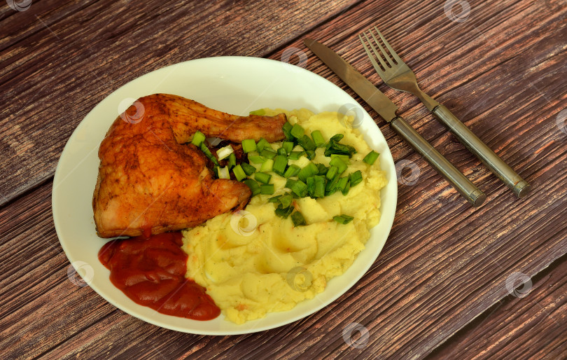 Скачать Картофельное пюре с мелко нарезанным зеленым луком и томатным соусом с запеченной куриной ножкой на столе из темного дерева. фотосток Ozero