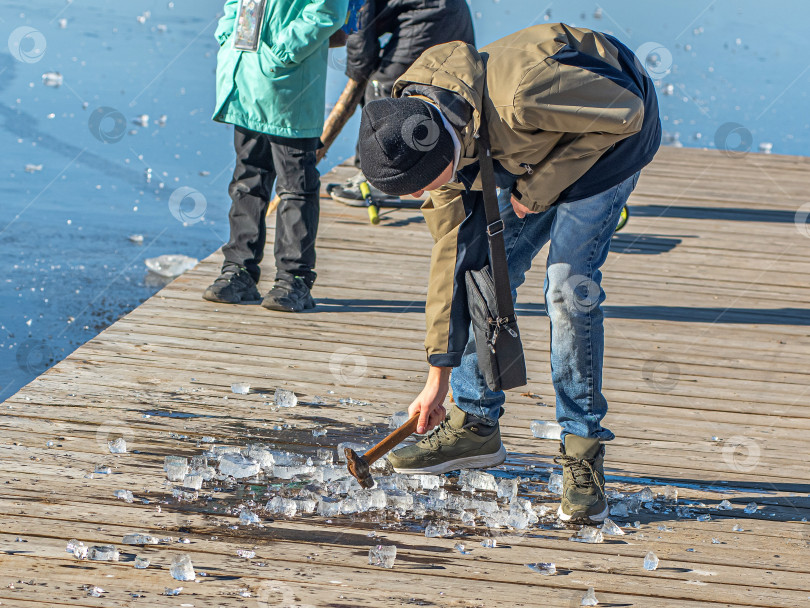 Скачать Россия,Сибирь 08 августа 2025 год. Дети играют и ломают лёд молотком на деревянном настиле. фотосток Ozero