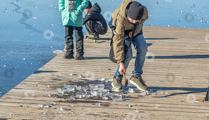 Скачать Россия,Сибирь 08 августа 2025 год. Дети играют и ломают лёд молотком на деревянном настиле. фотосток Ozero