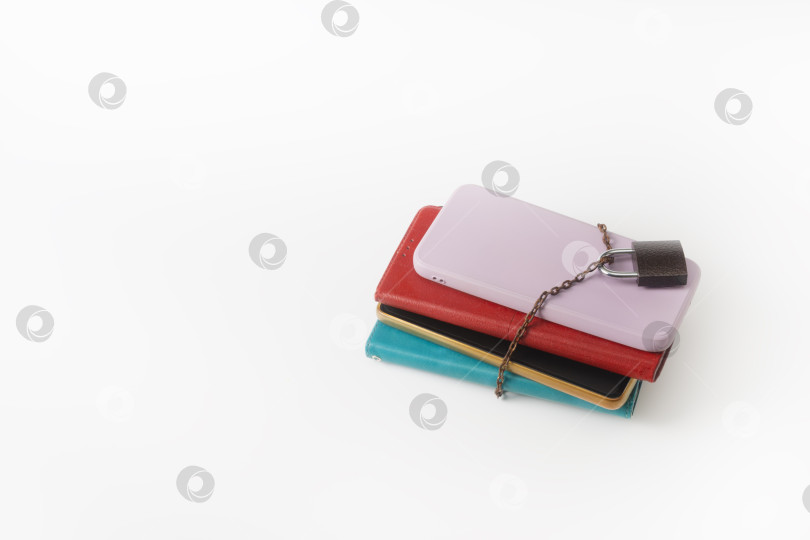 Скачать Несколько смартфонов, прикованных цепями и запертых на замок, на белом фоне. Цифровая перегрузка и усталость. Зависимость от гаджетов. фотосток Ozero