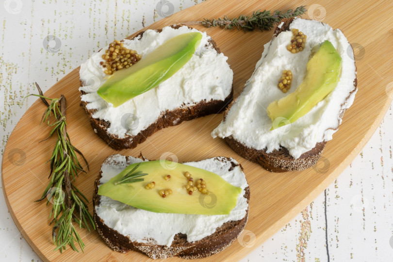 Скачать Вегетарианские сэндвичи с рикоттой и авокадо с зернистой горчицей на разделочной доске. Полезный перекус фотосток Ozero