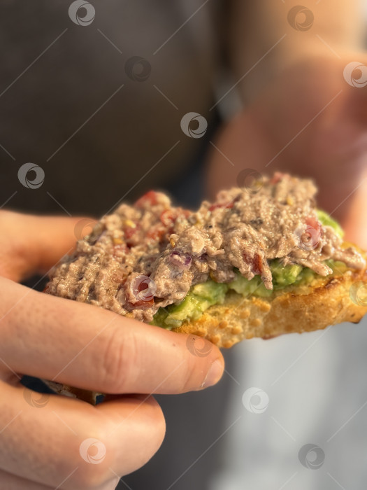 Скачать Руки, держащие открытый сэндвич с тунцом и авокадо на размытом фоне фотосток Ozero