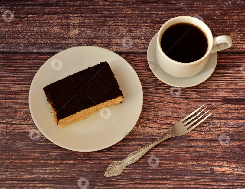 Скачать Кусочек итальянского десерта тирамису на деревянном столе, вилка и чашка горячего черного кофе на блюдце рядом. фотосток Ozero