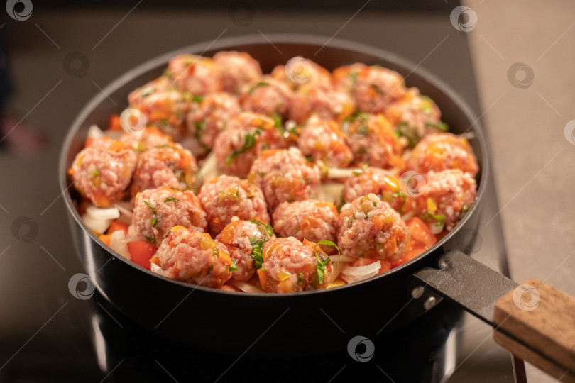 Скачать Мясные фрикадельки готовятся в сковороде на овощной подушке из репчатого лука, помидор и моркови фотосток Ozero