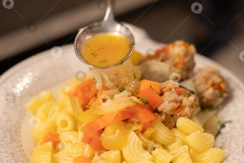 Скачать Готовое блюдо, мясные фрикадельки на пару из фарша с рисом и тушеными овощами в белой тарелке с гарниром из трубчатых макарон, приправленные специями. В ложке соус подливка готовая пролиться на вкусное блюдо. Столовый прибор в воздухе над едой. Здоровая аппетитная пища. фотосток Ozero