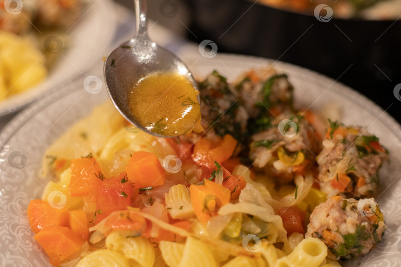 Скачать Готовое блюдо, мясные фрикадельки на пару из фарша с рисом и тушеными овощами в белой тарелке с гарниром из трубчатых макарон, приправленные специями. В ложке соус подливка готовая пролиться на вкусное блюдо. Столовый прибор в воздухе над едой. Здоровая вкусная пища. фотосток Ozero