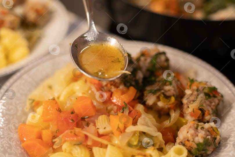 Скачать Готовое блюдо, мясные аппетитные фрикадельки на пару из фарша с рисом и тушеными овощами в белой тарелке с гарниром из трубчатых макарон, приправленные специями. В ложке соус подливка готовая пролиться на вкусное блюдо. Столовый прибор в воздухе над едой. Здоровая вкусная пища. фотосток Ozero