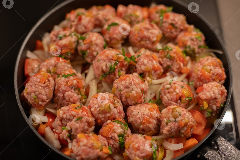 Скачать Мясные фрикадельки аппетитно готовятся в сковороде на овощной подушке из репчатого лука, помидор и моркови на индукционной плите фотосток Ozero