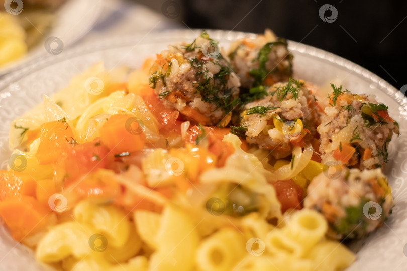 Скачать Мясные фрикадельки с макаронами, рожками, посыпанные мелко нарезанным свежим зеленым укропом аппетитно лежат на овощной подушке из репчатого лука, помидор и моркови на в белой тарелке фотосток Ozero