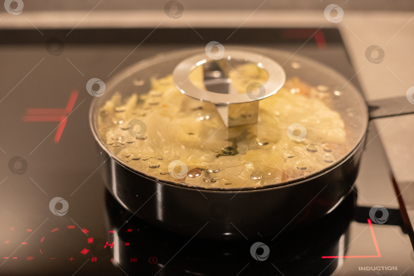 Скачать Сковорода под стеклянной крышкой на индукционной плите, внутри готовится тушится капуста фотосток Ozero