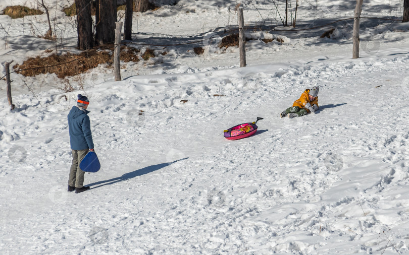 Скачать Россия, Красноярск 25 февраля 2025г. Мужчина с ребенком катаются со снежной горки фотосток Ozero