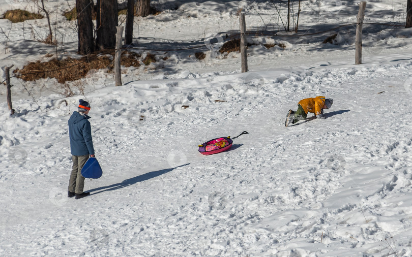 Скачать Россия, Красноярск 25 февраля 2025г. Мужчина с ребенком катаются со снежной горки фотосток Ozero