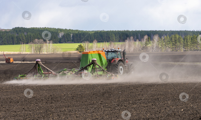 Скачать Весенние полевые работы, трактор с прицепной сеялкой сеет семена на сельскохозяйственном поле фотосток Ozero