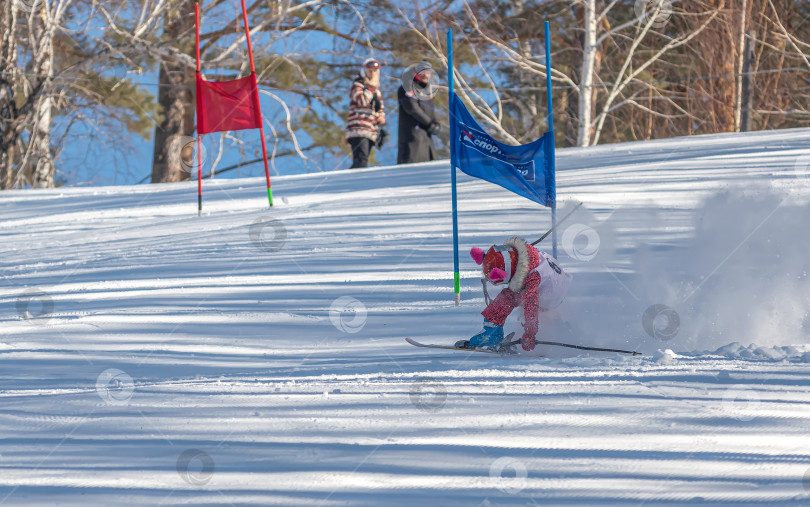 Скачать Россия, Красноярск 25 февраля 2025г.  Девочка лыжница,  падает на лыжах, катаясь  по снежному склону. фотосток Ozero