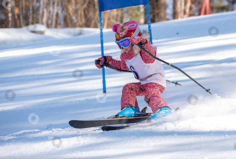 Скачать Россия, Красноярск 25 февраля 2025г. Маленькая девочка лыжница, спускается на лыжах по снежному склону. фотосток Ozero