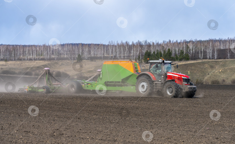 Скачать Весенне-полевые работы, трактор с прицепной сеялкой сеет семена на сельскохозяйственном поле фотосток Ozero