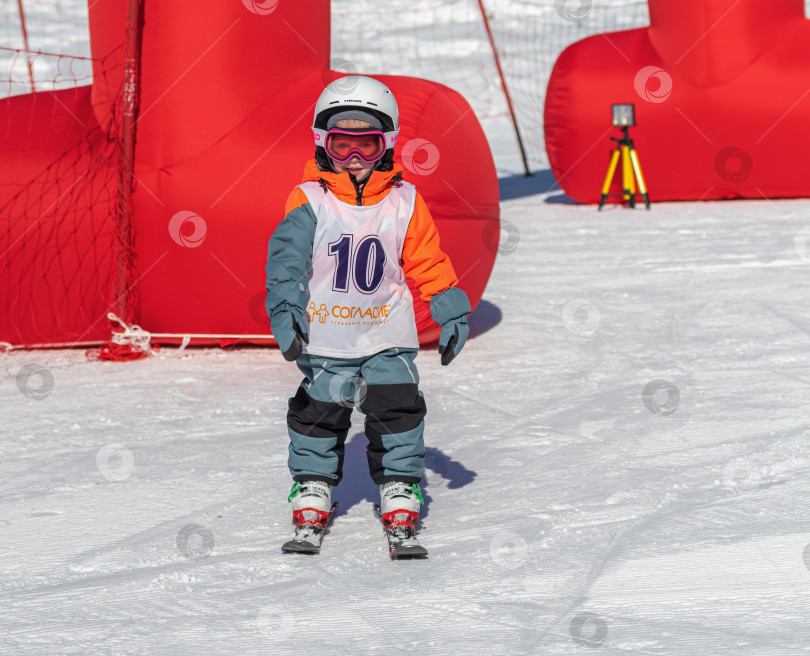 Скачать Россия, Красноярск 25 марта 2025г. Ребёнок в лыжной экипировке стоит на снегу. На нём шлем, защитные очки фотосток Ozero