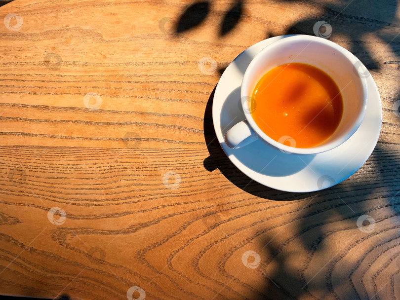 Скачать Вид сверху на белую чашку с облепиховым чаем на деревянном столе. Место для текста. Тени листьев, свет фотосток Ozero
