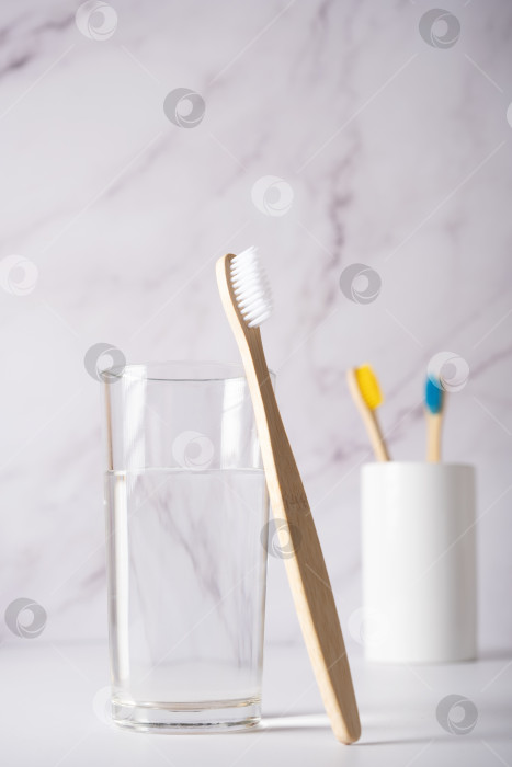 Скачать Бамбуковая зубная щетка с белой щетиной рядом со стаканом чистой воды. фотосток Ozero