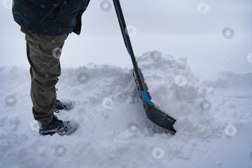 Скачать Мужчина в темной куртке разгребает снег лопатой возле дома, деревенская улица, зима, сугробы фотосток Ozero