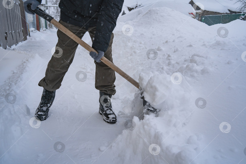 Скачать Мужчина в темной куртке разгребает снег лопатой возле дома, деревенская улица, зима, сугробы фотосток Ozero