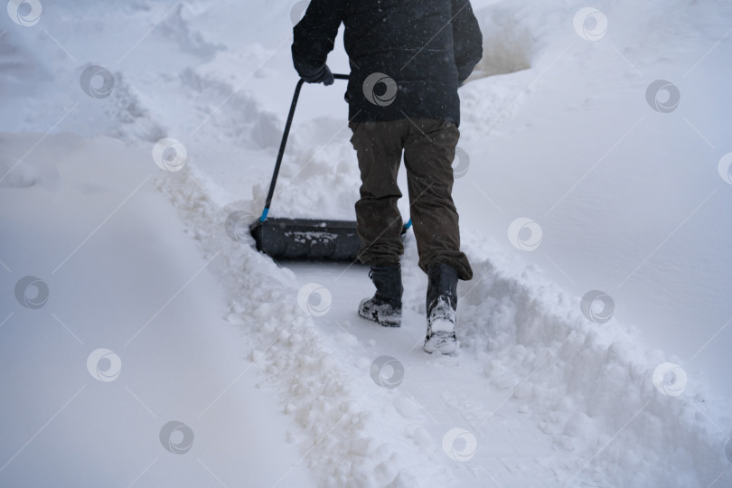 Скачать Мужчина в темной куртке разгребает снег лопатой возле дома, деревенская улица, зима, сугробы фотосток Ozero