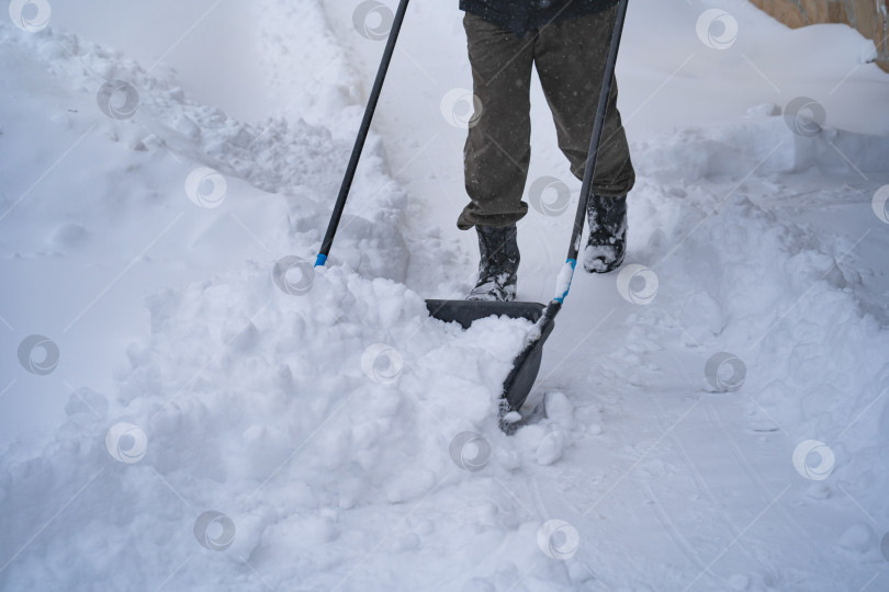 Скачать Мужчина в темной куртке разгребает снег лопатой возле дома, деревенская улица, зима, сугробы фотосток Ozero
