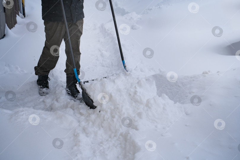 Скачать Мужчина в темной куртке разгребает снег лопатой возле дома, деревенская улица, зима, сугробы фотосток Ozero