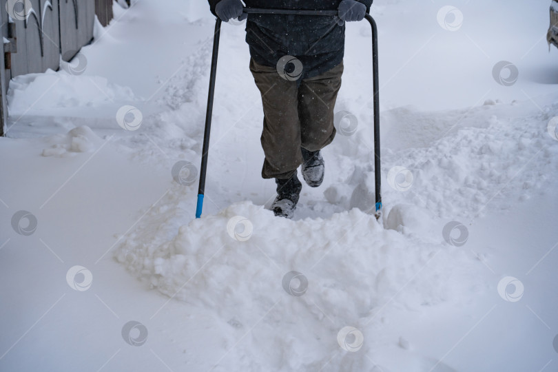 Скачать Мужчина в темной куртке разгребает снег лопатой возле дома, деревенская улица, зима, сугробы фотосток Ozero