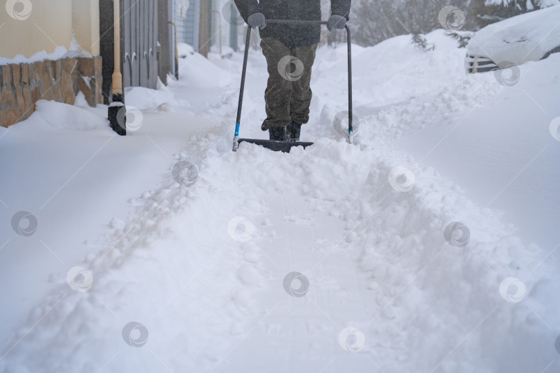 Скачать Мужчина в темной куртке разгребает снег лопатой возле дома, деревенская улица, зима, сугробы фотосток Ozero