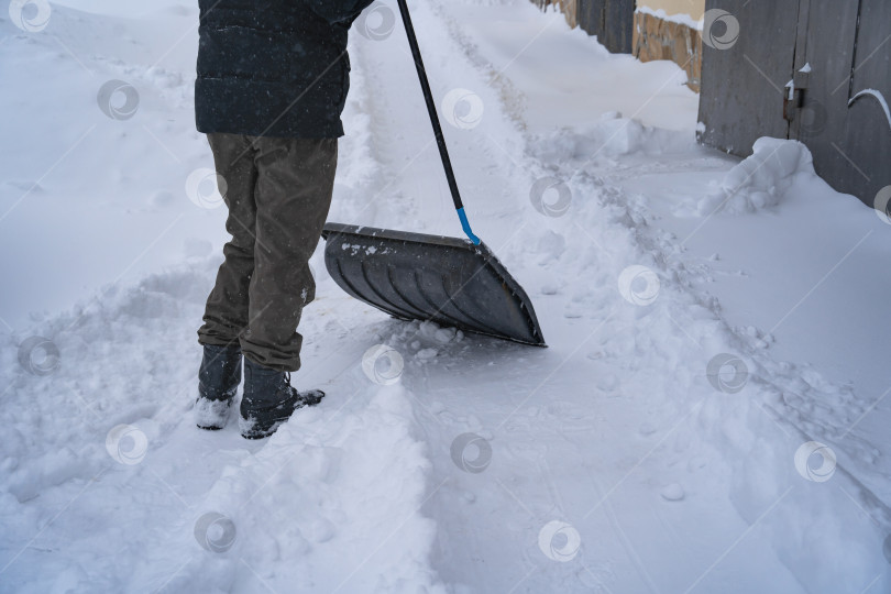 Скачать Мужчина в темной куртке разгребает снег лопатой возле дома, деревенская улица, зима, сугробы фотосток Ozero