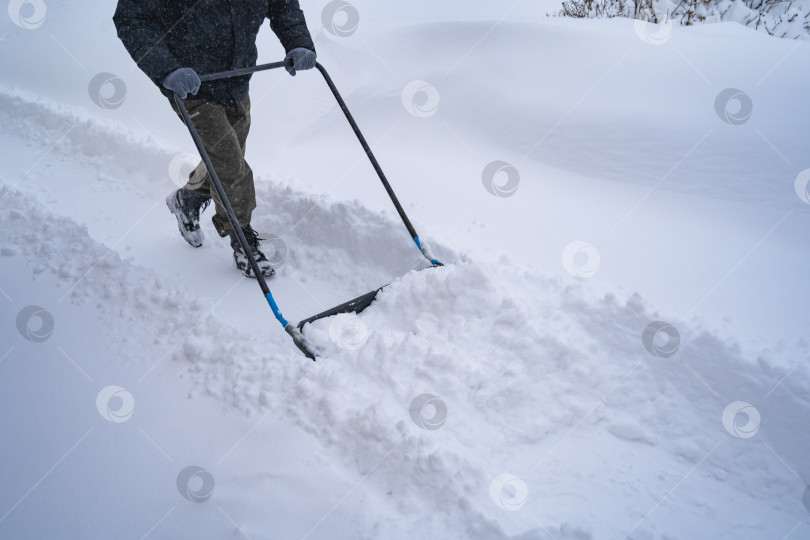 Скачать Мужчина в темной куртке разгребает снег лопатой возле дома, деревенская улица, зима, сугробы фотосток Ozero