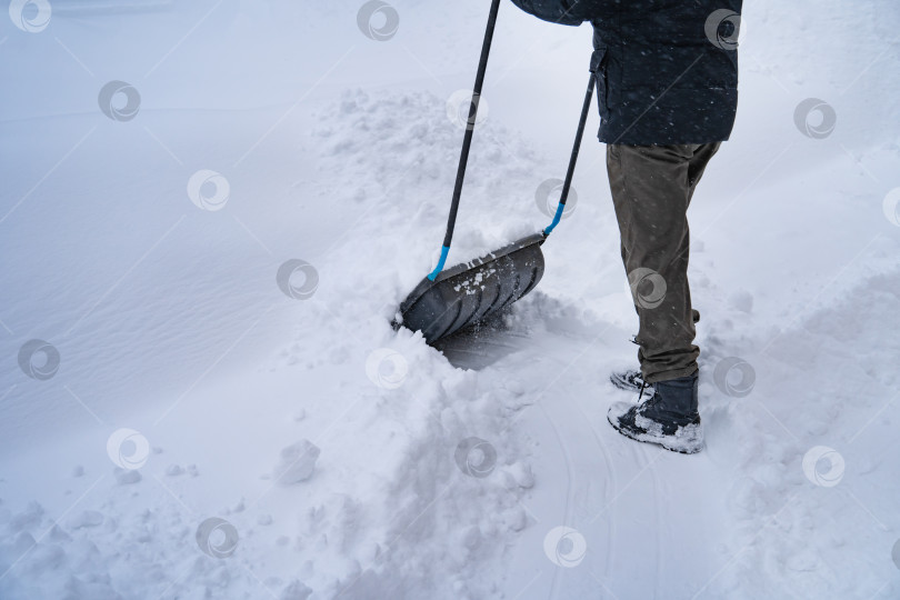 Скачать Мужчина в темной куртке разгребает снег лопатой возле дома, деревенская улица, зима, сугробы фотосток Ozero
