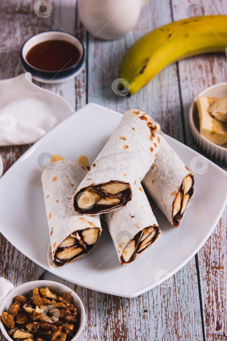 Скачать Покрытые шоколадом ломтики банана, завернутые в тортилью, на тарелке на столе, вид сверху фотосток Ozero