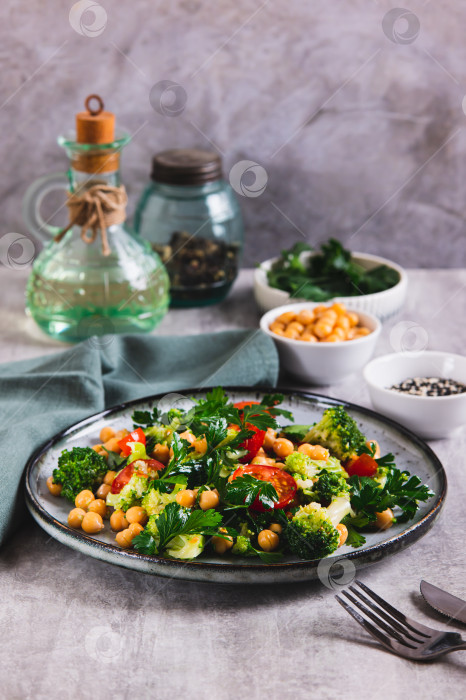 Скачать Вегетарианский салат с нутом, помидорами, брокколи и зеленью на тарелке на столе в вертикальном положении фотосток Ozero