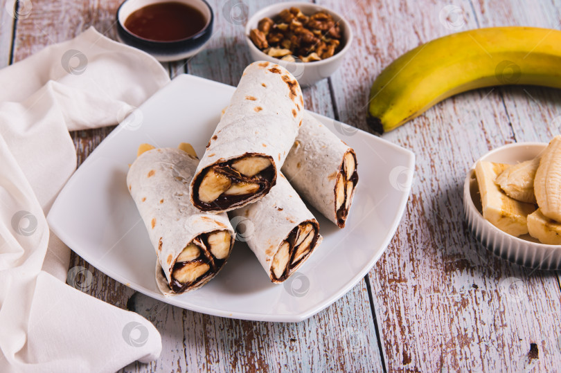 Скачать Покрытые шоколадом ломтики банана, завернутые в тортилью, на тарелке на столе фотосток Ozero
