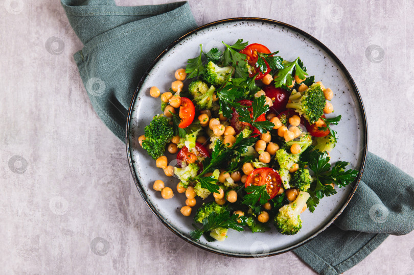 Скачать Крупный план салата с нутом, помидорами, брокколи и зеленью на тарелке на столе, вид сверху фотосток Ozero