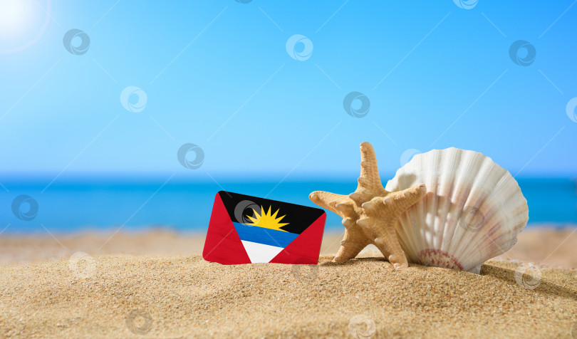 Скачать Тропический пляж с ракушками и флагом Антигуа и Барбуды. Концепция райского отдыха на пляжах Антигуа и Барбуды. фотосток Ozero