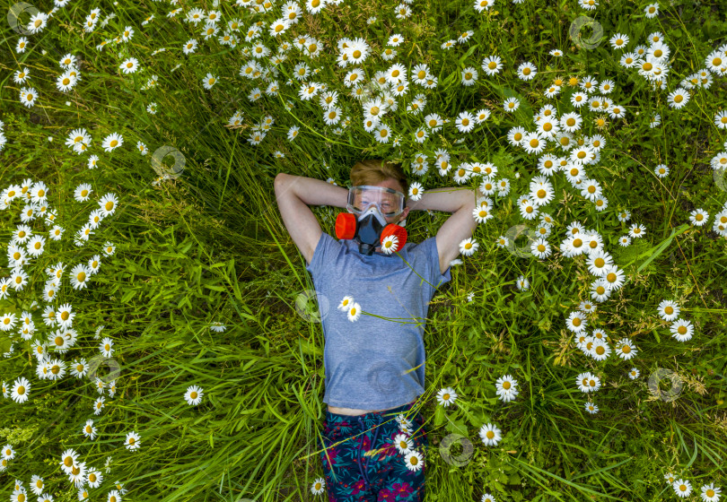 Скачать человек с аллергией в респираторе и защитных очках лежит на поле маргариток и наслаждается ароматом свежего воздуха фотосток Ozero
