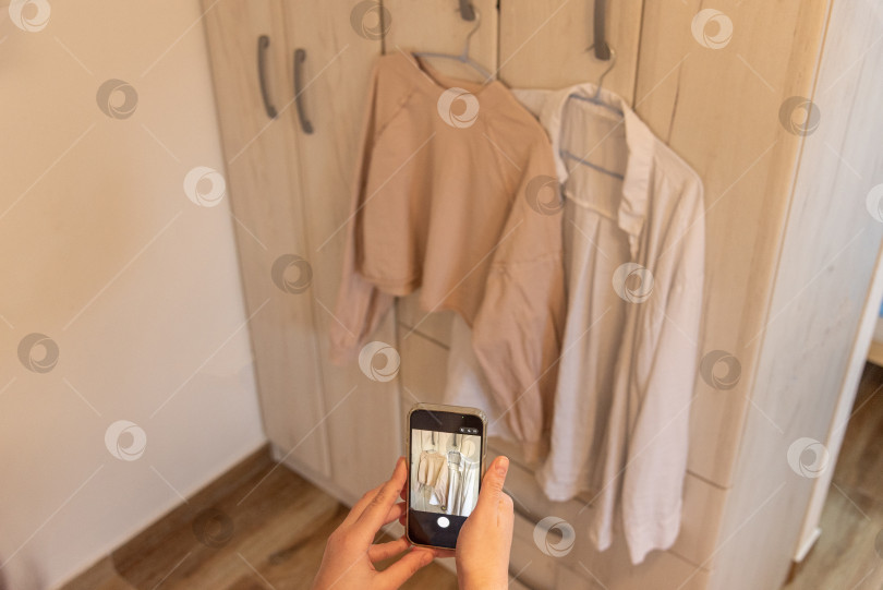 Скачать Женщина фотографирует на телефон старую одежду продает жертвует концепция осознанного потребления фотосток Ozero