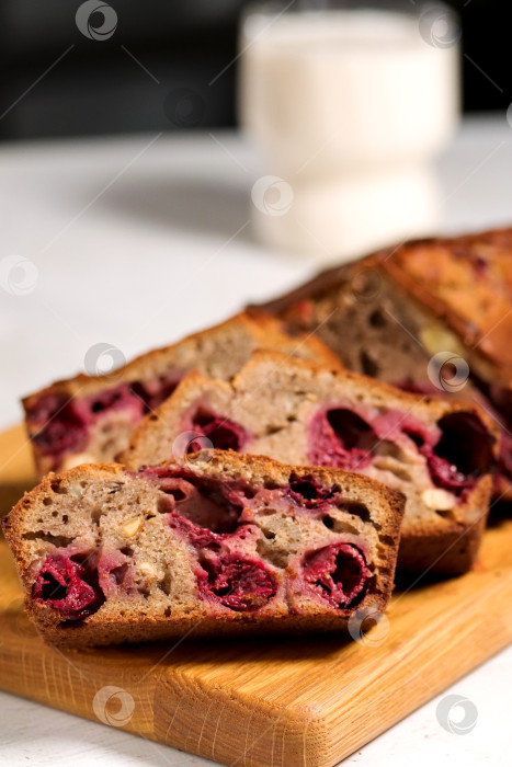 Скачать Сладкий хлеб с начинкой из ягод вишни нарезают ломтиками и выкладывают на деревянную доску. На заднем плане изображен стакан молока. В этой сцене показано простое приготовление вкусной закуски. фотосток Ozero