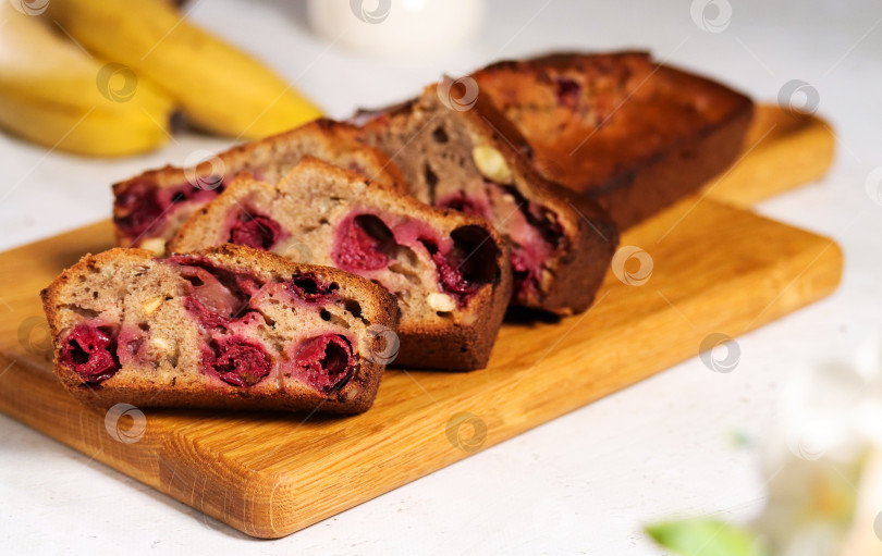 Скачать На деревянной доске разложены ломтики бананового хлеба с вишней. На заднем плане кухни - свежие бананы, изображающие домашнюю выпечку. Полезное блюдо для семейного завтрака фотосток Ozero