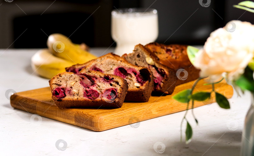 Скачать На деревянной разделочной доске можно испечь вкусный сладкий хлеб с золотистой корочкой, подать к столу со свежими фруктами и прохладительным напитком. Ломтики бананового хлеба с кусочками вишни фотосток Ozero
