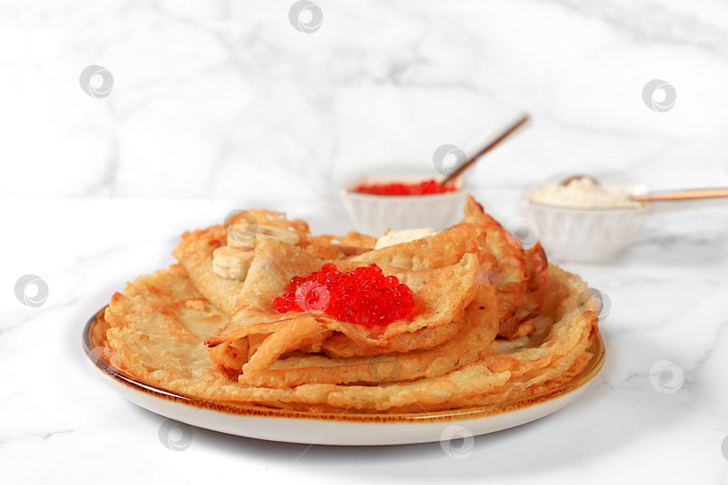 Скачать Вкусные русские блинчики с мягким сыром, бананами и красной икрой на кухонном столе. Полезный завтрак, приготовленный из свежих продуктов, вдохновленный Масленицей и традиционной русской кухней фотосток Ozero