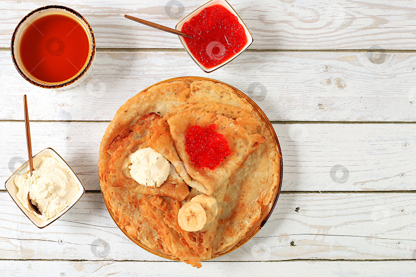 Скачать Вкусные русские блинчики с мягким сыром, бананами и медом на кухонном столе. Полезный завтрак из свежих продуктов в стиле Масленицы и традиционной русской кухни фотосток Ozero