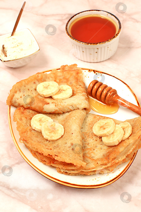 Скачать Вкусные русские блинчики с мягким сыром, бананами и медом на мраморном столе. Полезный завтрак, приготовленный из свежих продуктов, вдохновленный Масленицей и традиционной русской кухней фотосток Ozero
