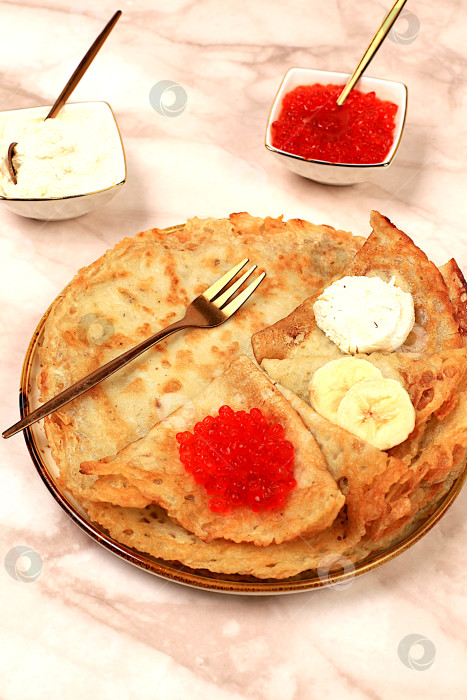 Скачать Вкусные русские блинчики с мягким сыром, бананами и красной икрой на мраморном столе. Полезный завтрак из свежих продуктов, масленичная концепция и традиционная русская кухня, особый акцент фотосток Ozero